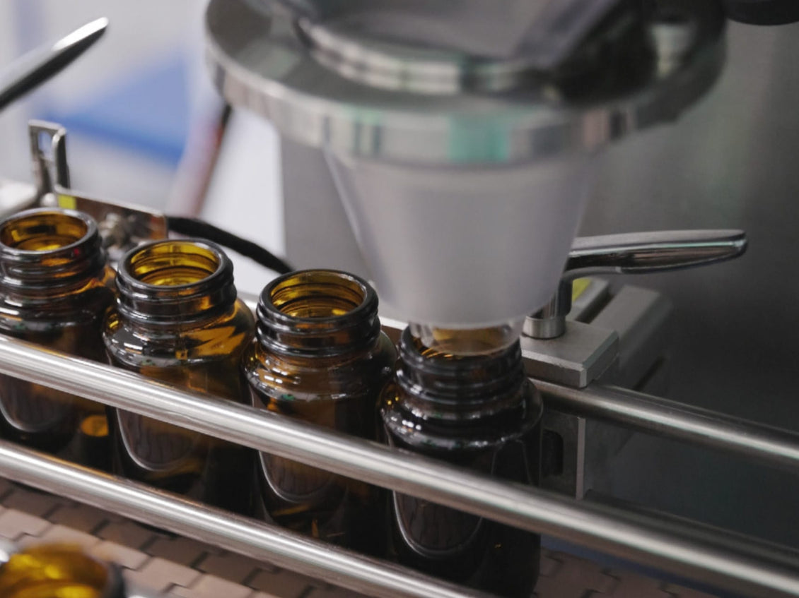 Automated machine dispensing liquid into small brown bottles.