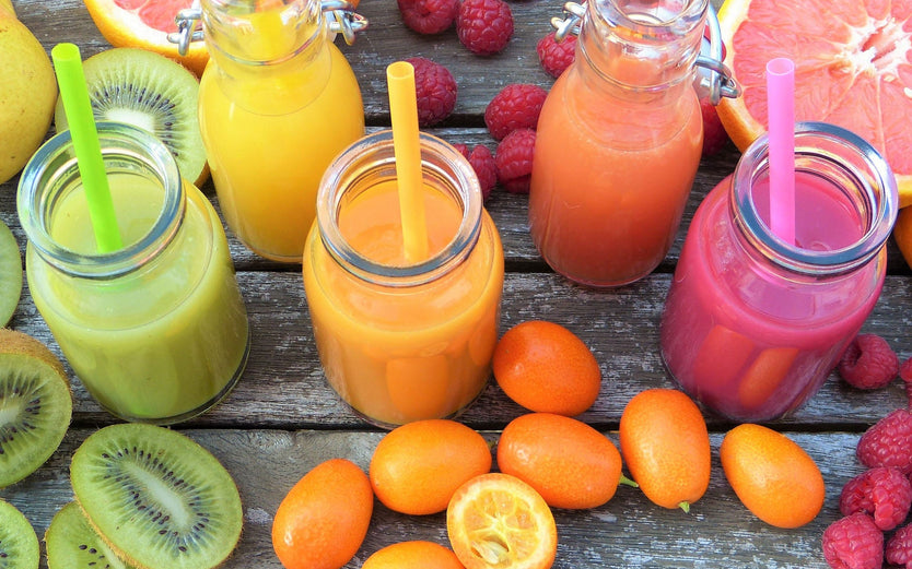 Green, orange and pink coloured smoothies and fruits on a wooden table
