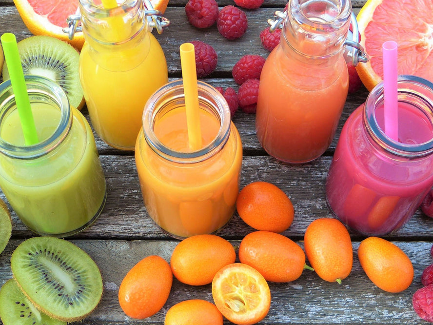 Green, orange and pink coloured smoothies and fruits on a wooden table