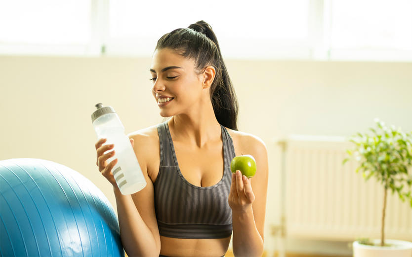 Women on a yoga mat holding a water bottle and apple