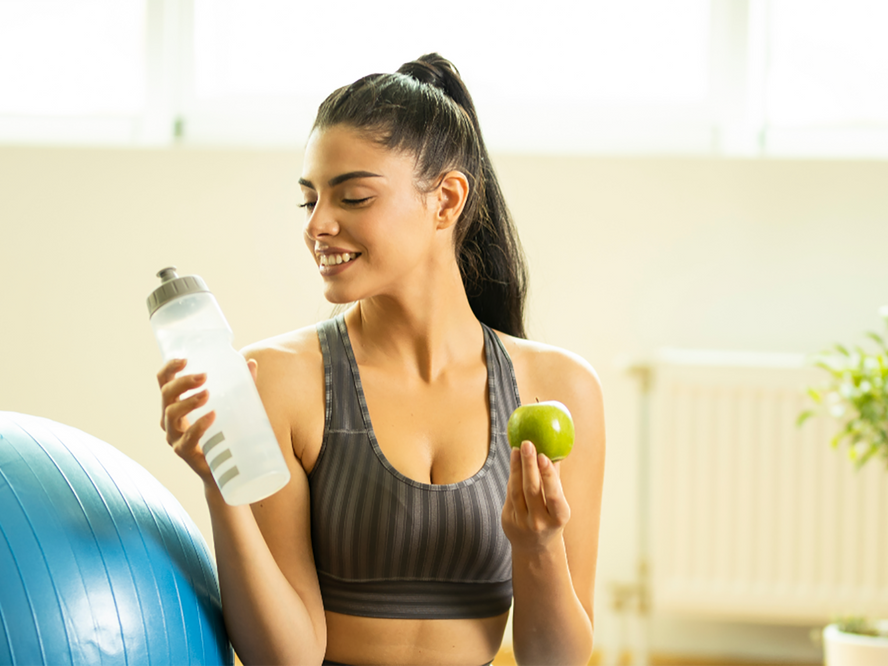 Women on a yoga mat holding a water bottle and apple