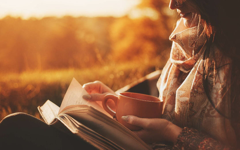 Woman reading a book outside with a mug