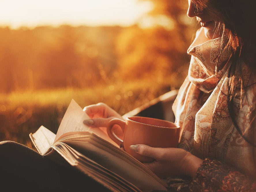 Woman reading a book outside with a mug