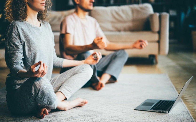 Two people meditating in front of a laptop
