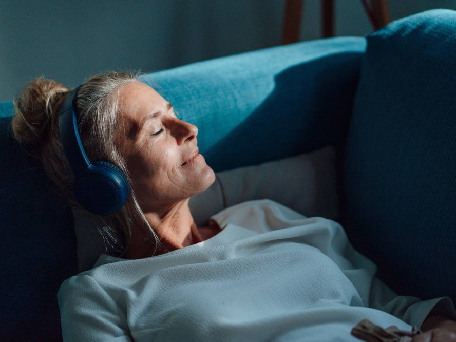Older woman relaxing on the couch listening to music through headphones