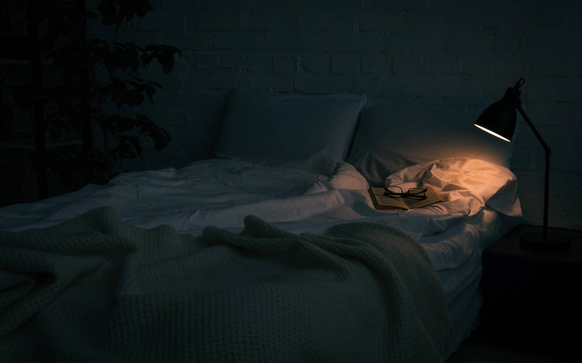 Dark room with lamp on and unmade bed