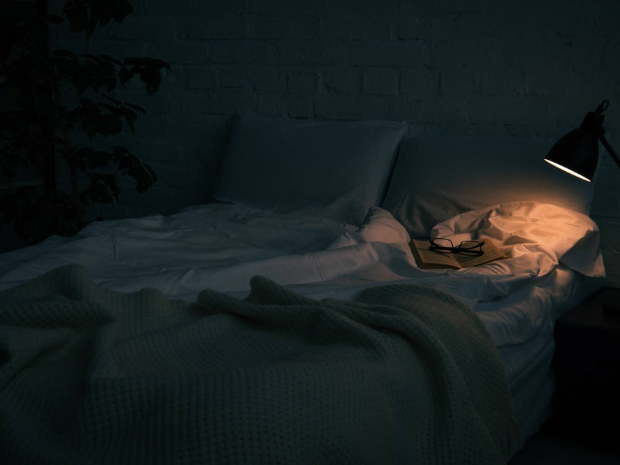 Dark room with lamp on and unmade bed