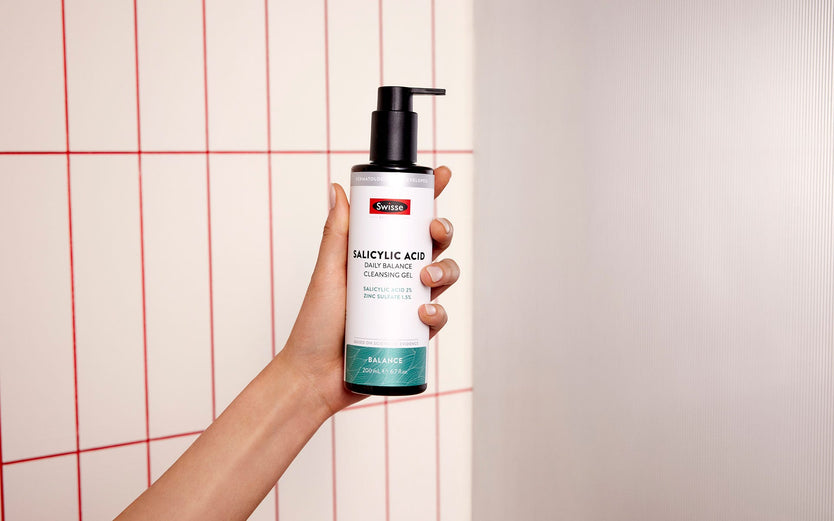 Hand holding Swisse Skincare Salicylic Acid Daily Balance Cleansing Gel in a bathroom