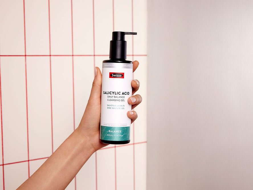 Hand holding Swisse Skincare Salicylic Acid Daily Balance Cleansing Gel in a bathroom