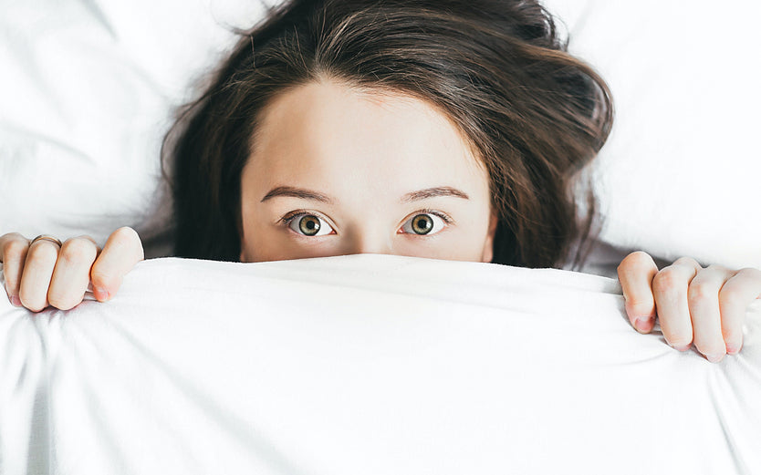 A woman in bed with sheets pulled up to cover half her face