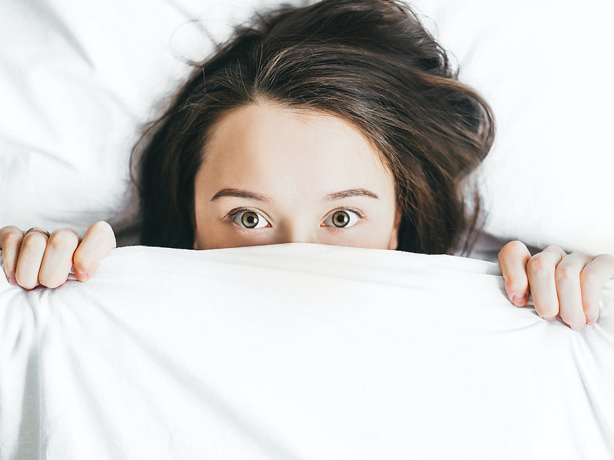 A woman in bed with sheets pulled up to cover half her face