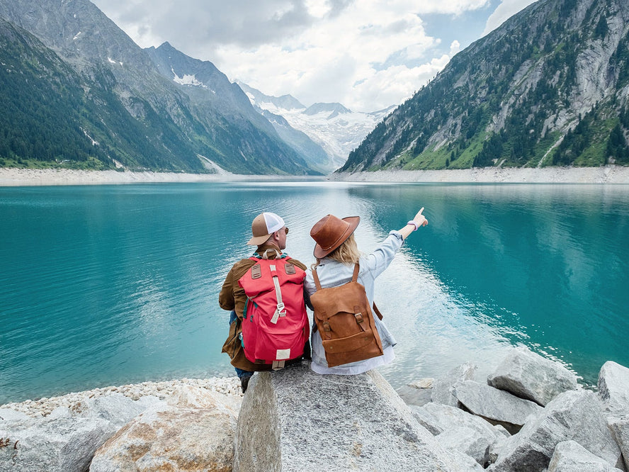 Two people sitting in front of a lake surrounded by mountains.