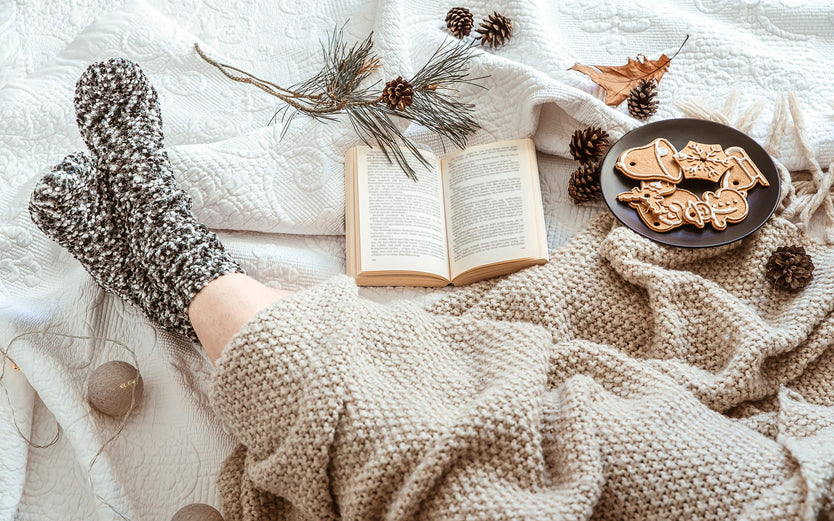 A person's legs in winter socks and a blanket, with a book and some Christmas biscuits
