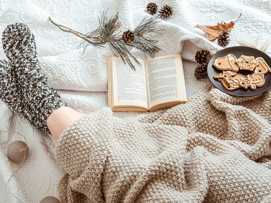 A person's legs in winter socks and a blanket, with a book and some Christmas biscuits
