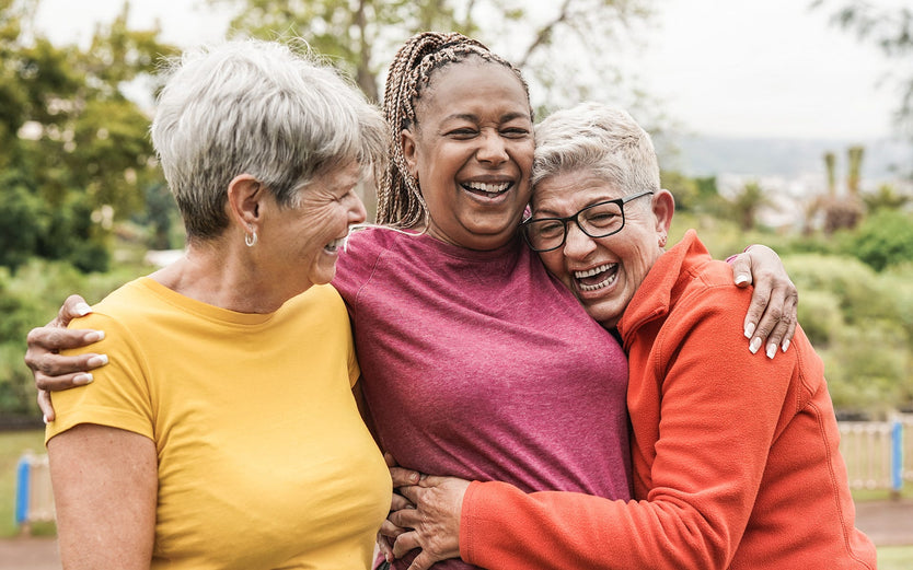 Three older women in activewear hugging and laughing