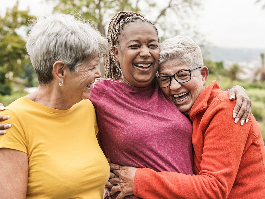 Three older women in activewear hugging and laughing
