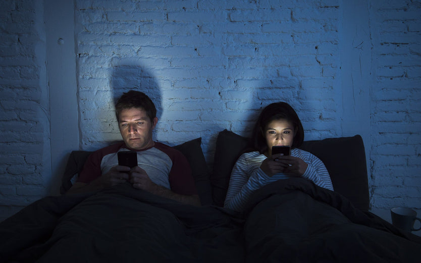 Man and women in bed looking at their mobile phones
