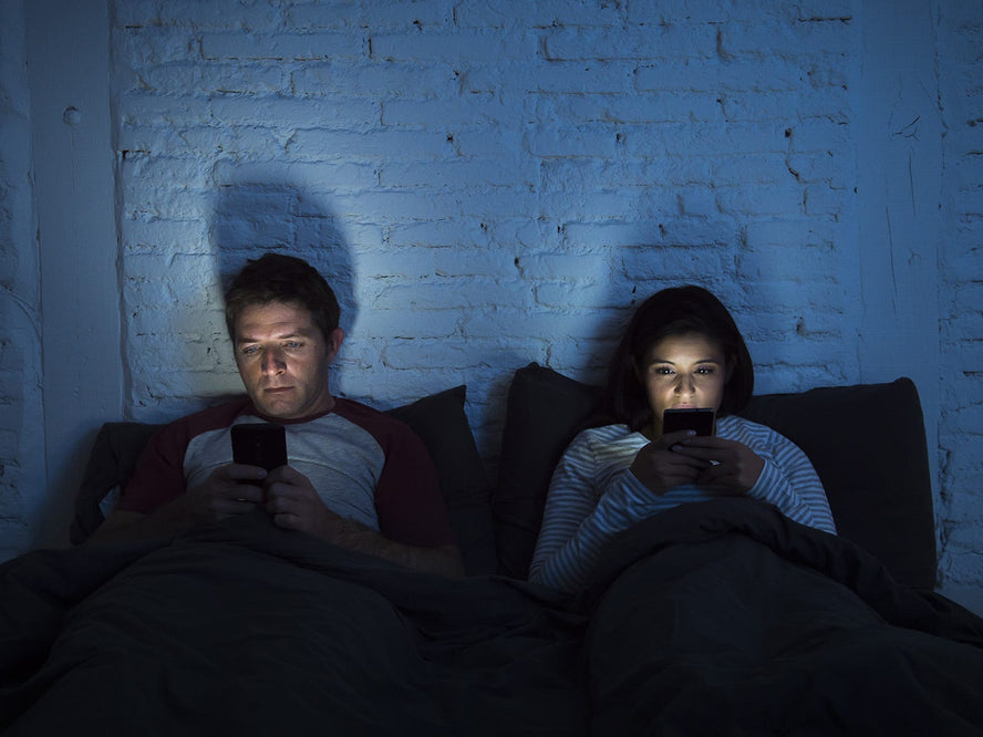 Man and women in bed looking at their mobile phones