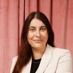 Person with long hair wearing a white blazer against a pink curtain background