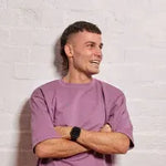 Man wearing a purple shirt with arms crossed against a light gray background