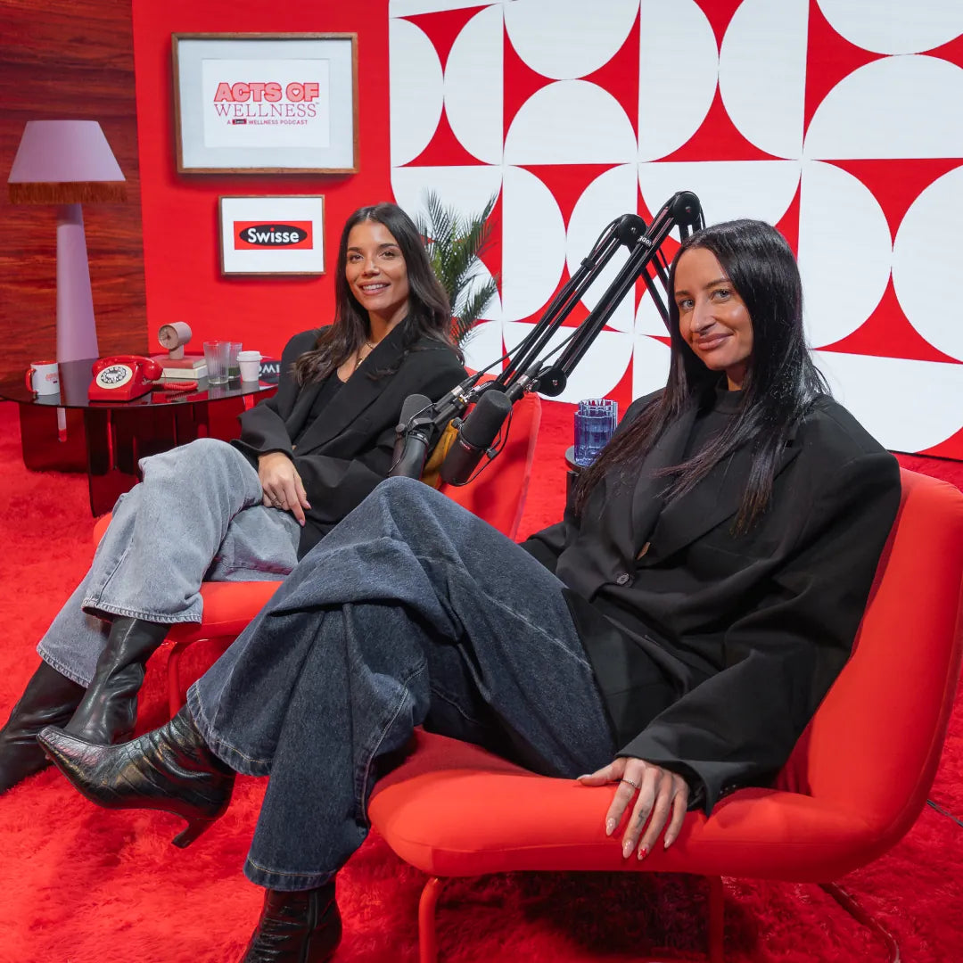 Two women sitting on a red couch in a studio with a red and white geometric patterned wall.