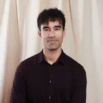 Man wearing a black shirt against a beige curtain background