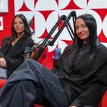 Two women sitting on a red couch with a microphone, likely in a podcast or interview setting.