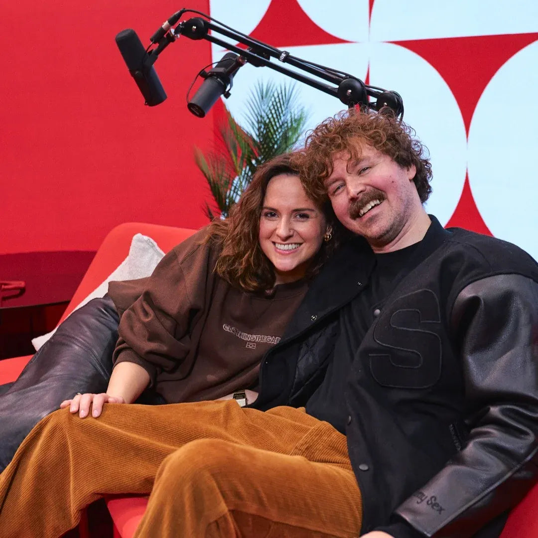 Two people sitting together with a microphone and camera setup against a colorful background