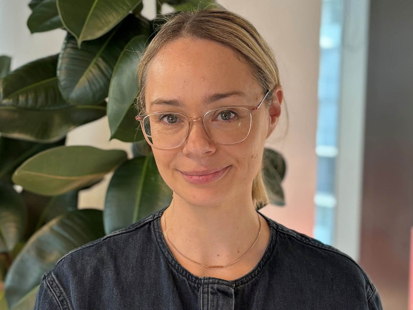 Woman wearing glasses and a black top in front of a plant