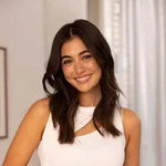 Woman in a white sleeveless top standing indoors with a neutral background