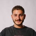 Man with a beard and short hair wearing a dark gray shirt against a plain background