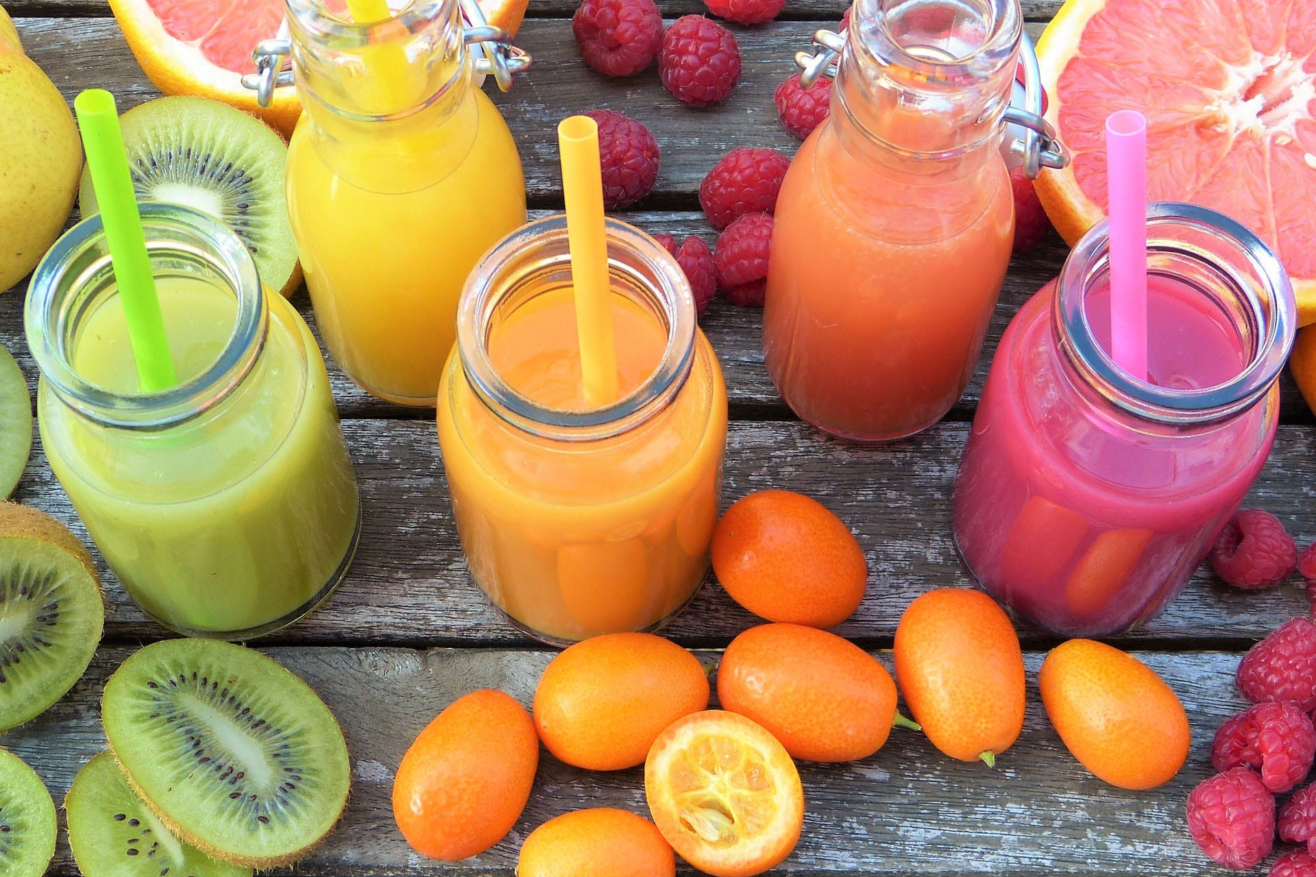 Green, orange and pink coloured smoothies and fruits on a wooden table