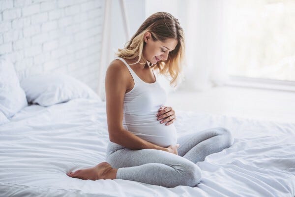 Pregnant woman on bed holding stomach