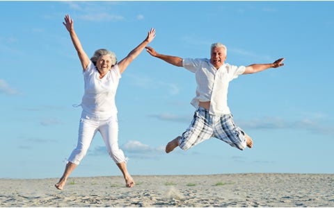 Older people doing a star jump on a beach