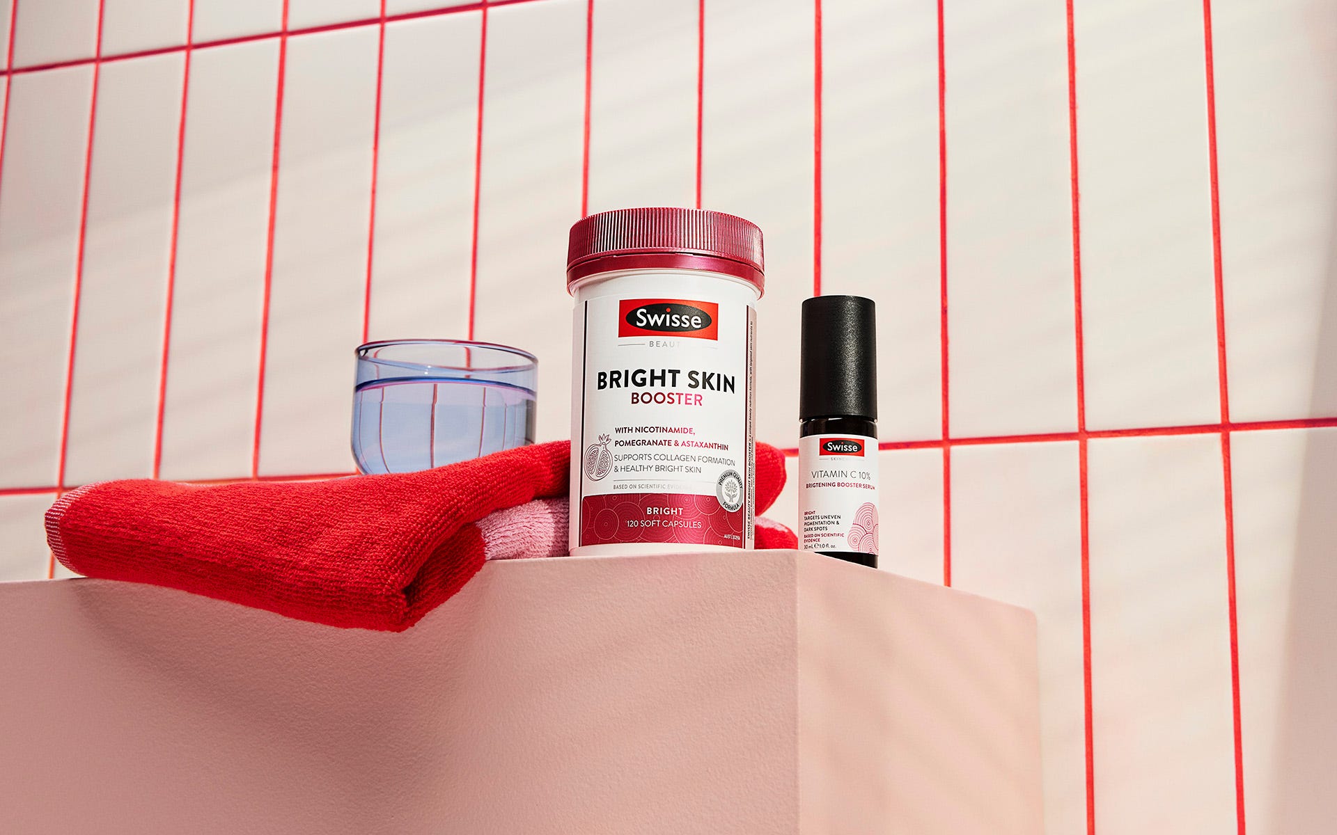 Two Swisse Beauty products from the Bright range next to a red towel and a glass of water.