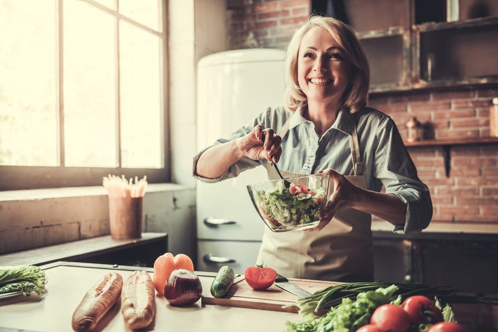 Happy woman making salad in kitchen