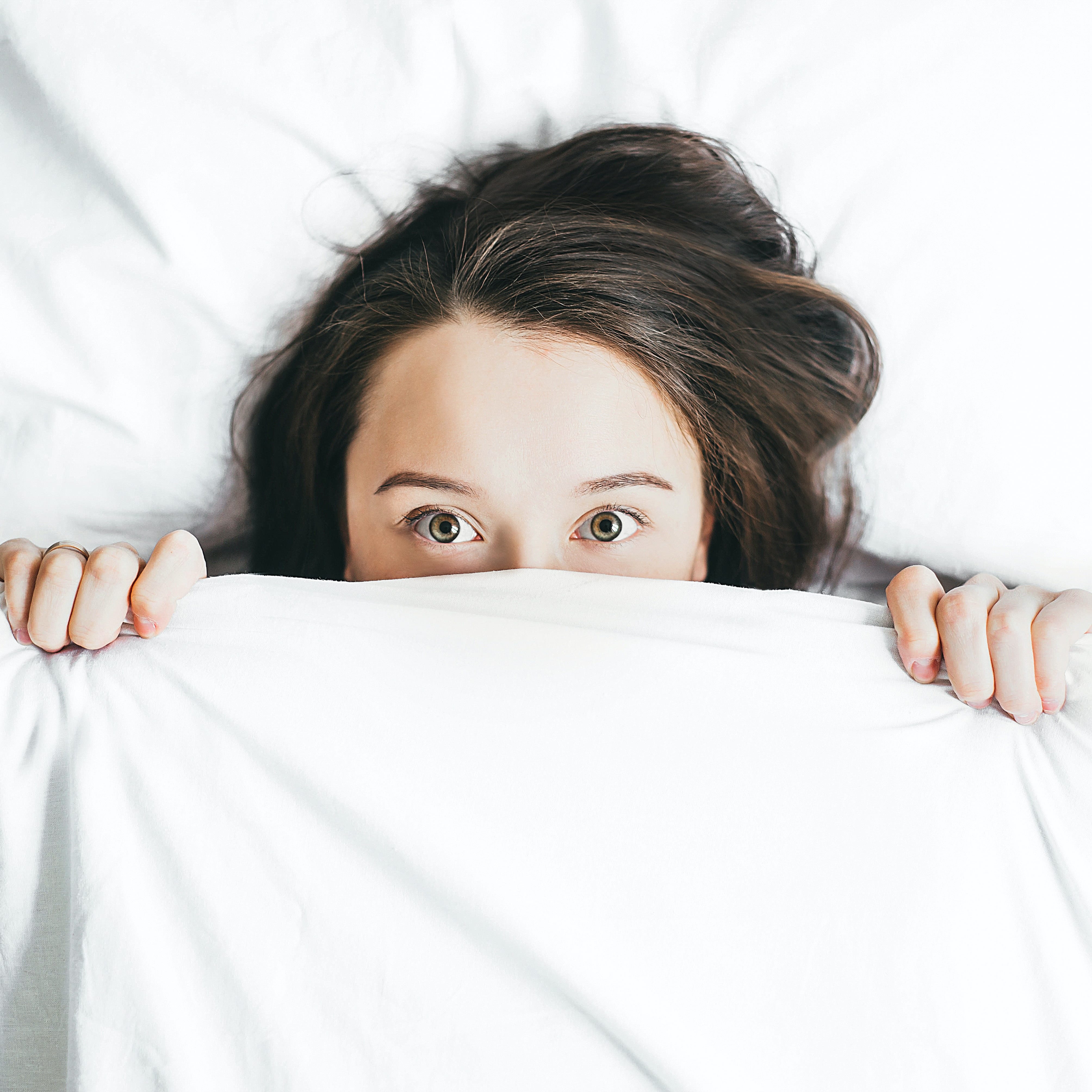 A woman in bed with sheets pulled up to cover half her face