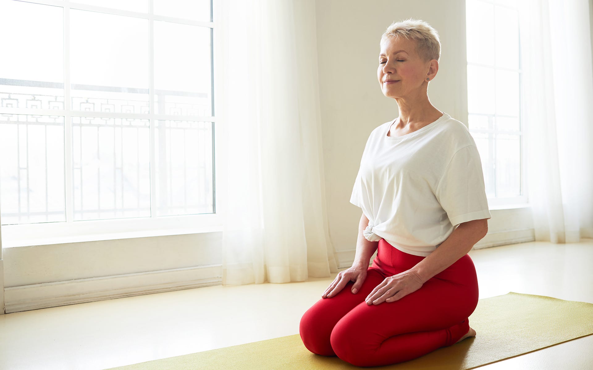 Women in yoga clothes kneeling on a mat and smiling